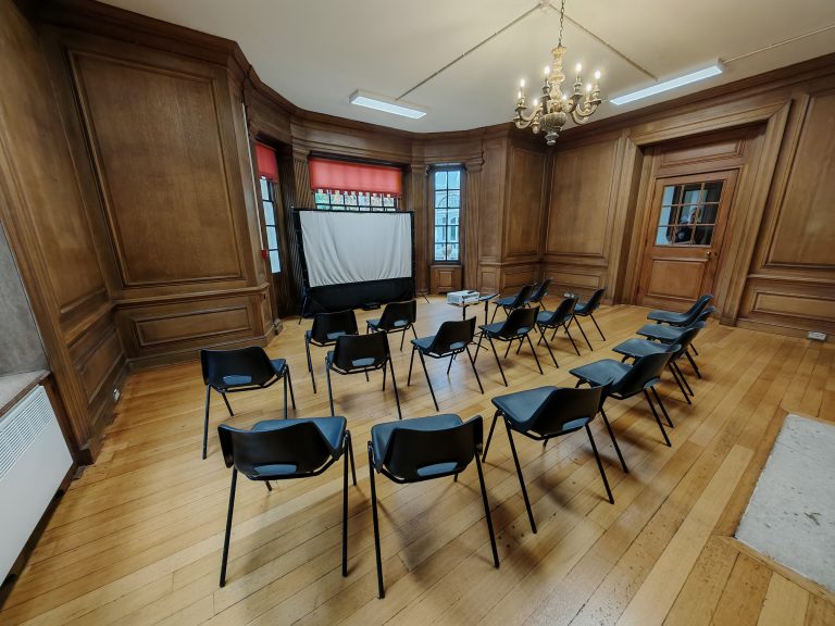 An elegant wood panelled room with conference chairs arranged in a semicircle around a projector screen